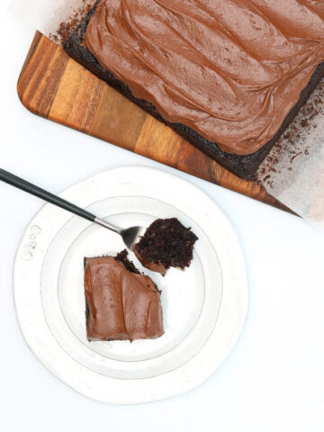 Square piece of chocolate zucchini cake with a forkful of cake on the plate, next to the chocolate cake.