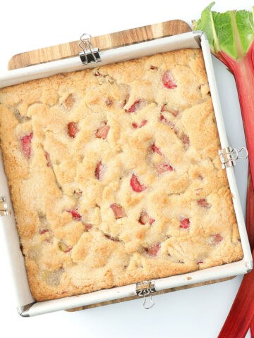 9x9 square baking pan with rhubarb cream snacking cake baked with 2 full stalks of rhubarb resting next to the pan.