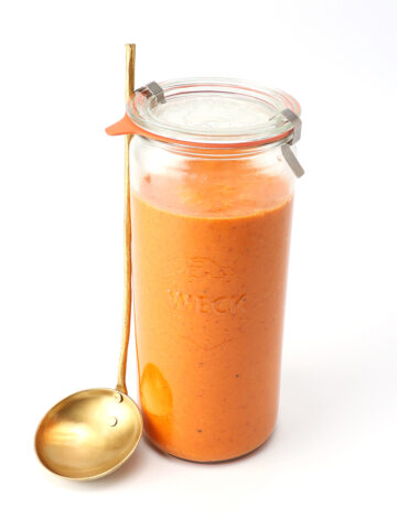 Roasted Red Pepper Dressing in a tall glass jar with a ladle propped against it.
