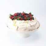 Pavlova on a cake stand with fresh strawberries garnished over top.