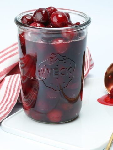 Cherry sauce in a glass wex jar with a ladle with cherry sauce laying next to it.