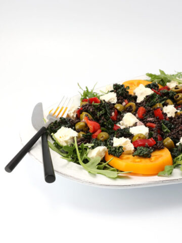 Partial view of a mediterranean black lentil salad on a serving platter with a fork and knife resting on the edge.