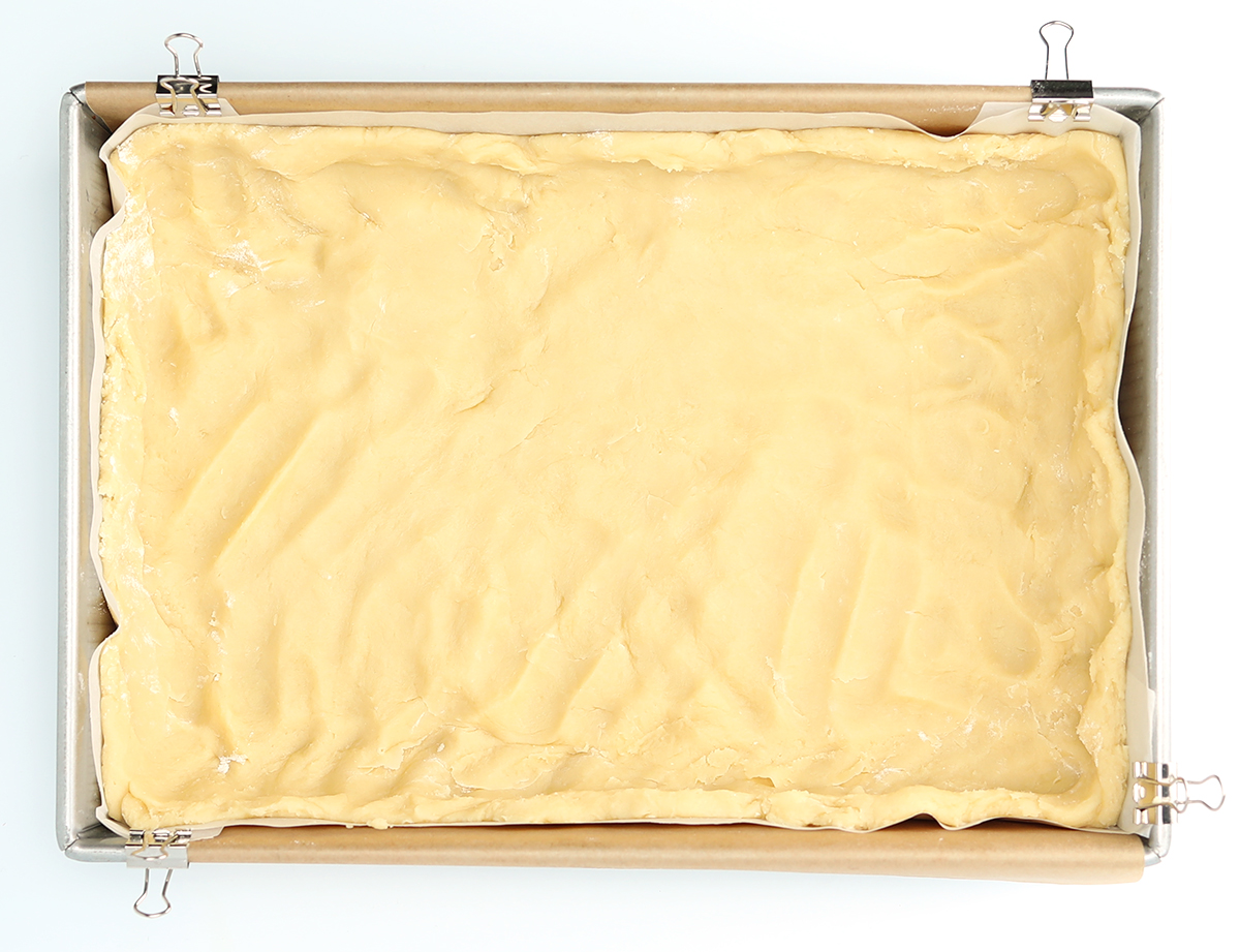 Pecan pie bar dough on parchment paper over a baking sheet.