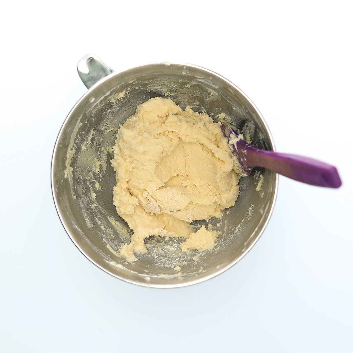 Shortbread dough in a mixing bowl with a purple spoon.