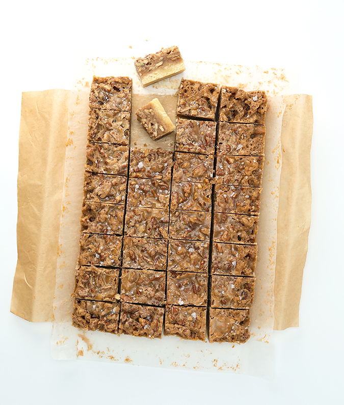 Top view of pecan pie bars on parchment paper, cut into squares with two of them pulled away on their side to reveal the layers.