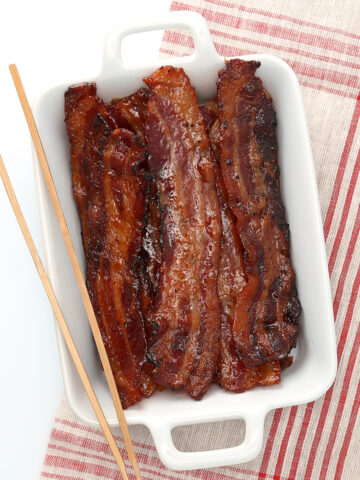 candied bacon in porcelain dish with wood tongs