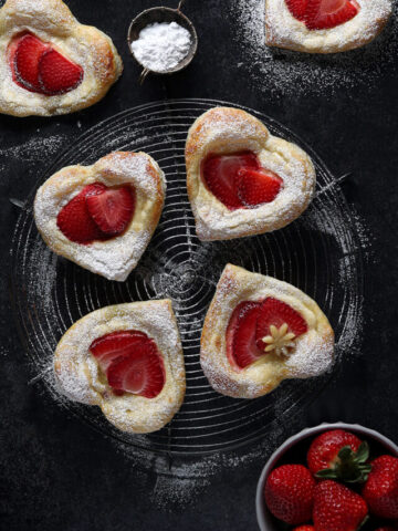 Strawberry Cream Cheese Puff Pastry Hearts dusted with powdered sugar on a cooling rack.