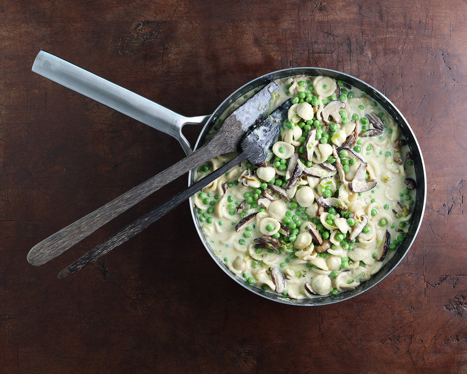 Serving utensils resting in a saucepan with fresh pea shiitake orecchiette pasta, ready to serve.