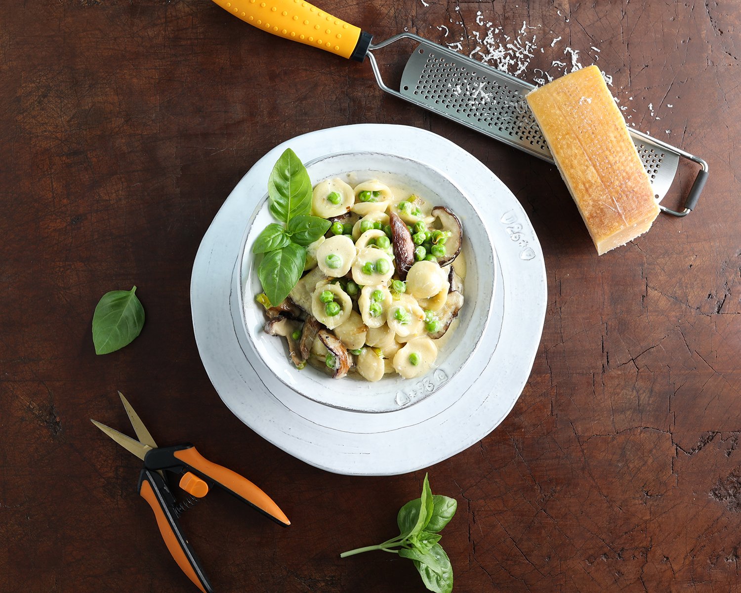 Top view of a bowl of fresh pea shiitake orecchiette pasta with fresh parmesan block and a microplane.
