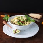 Spoonful of fresh pea shiitake orecchiette pasta resting on a small plate holding a bowl of the freshly made pasta and mushrooms with peas.