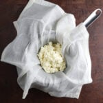 Homemade ricotta cheese resting on a cheesecloth over a pot.