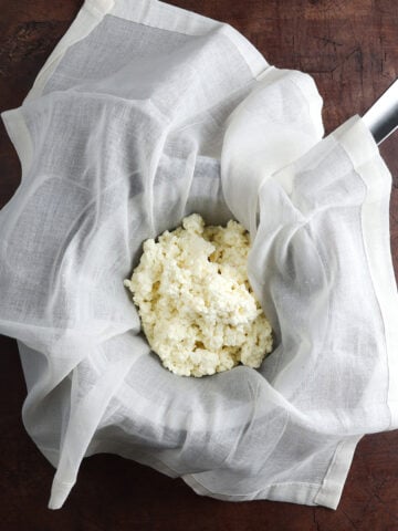 Homemade ricotta cheese resting on a cheesecloth over a pot.