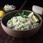 Fresh parmesan grated over a large wooden bowl of lemon ricotta orzo with baby peas.