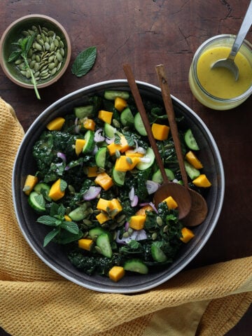Top view of the kale mango chopped salad with the dressing in a small glass bowl and small dish of pepitas next to it.