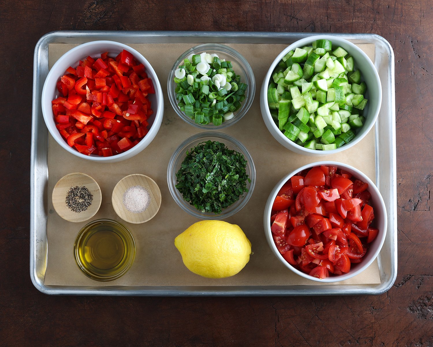 Chopped ingredients in dishes with the fresh dressing ingredients laid out on a baking sheet to prepare a Jerusalem salad.