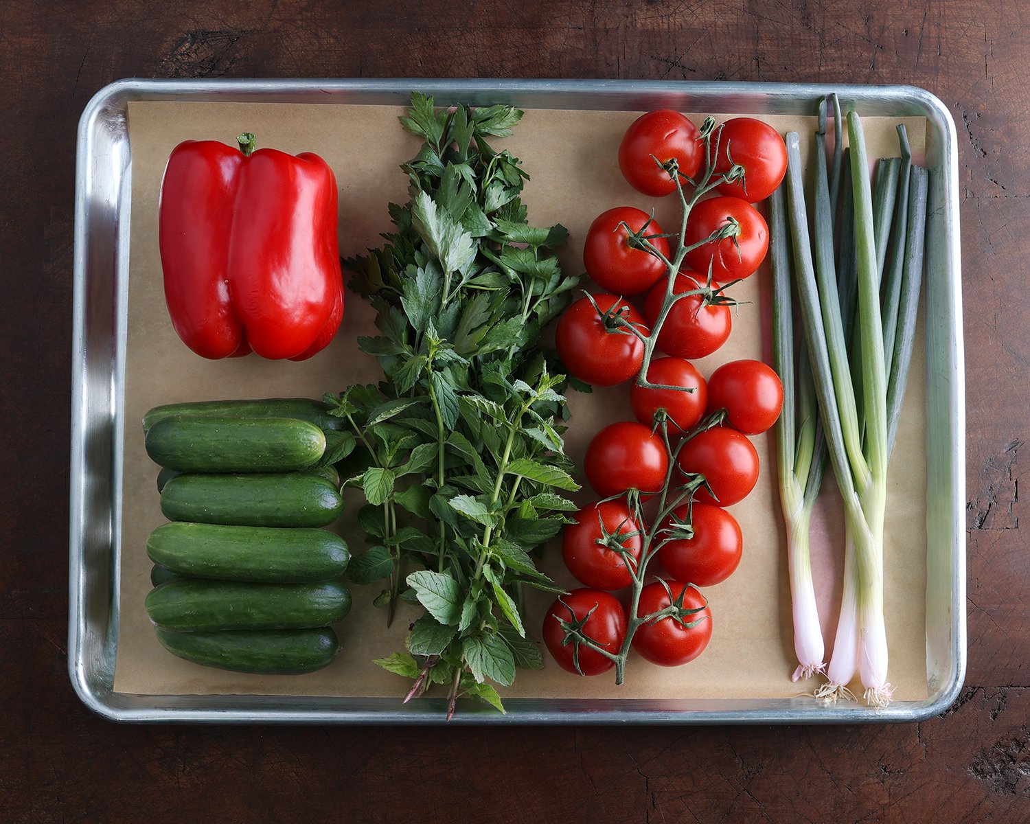 Fresh ingredients used to prepare a Jerusalem salad laid out on a baking sheet.