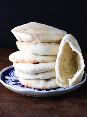 A pita pocked sliced into to show the inside bread leaning against a stack of pitas on a blue plate.