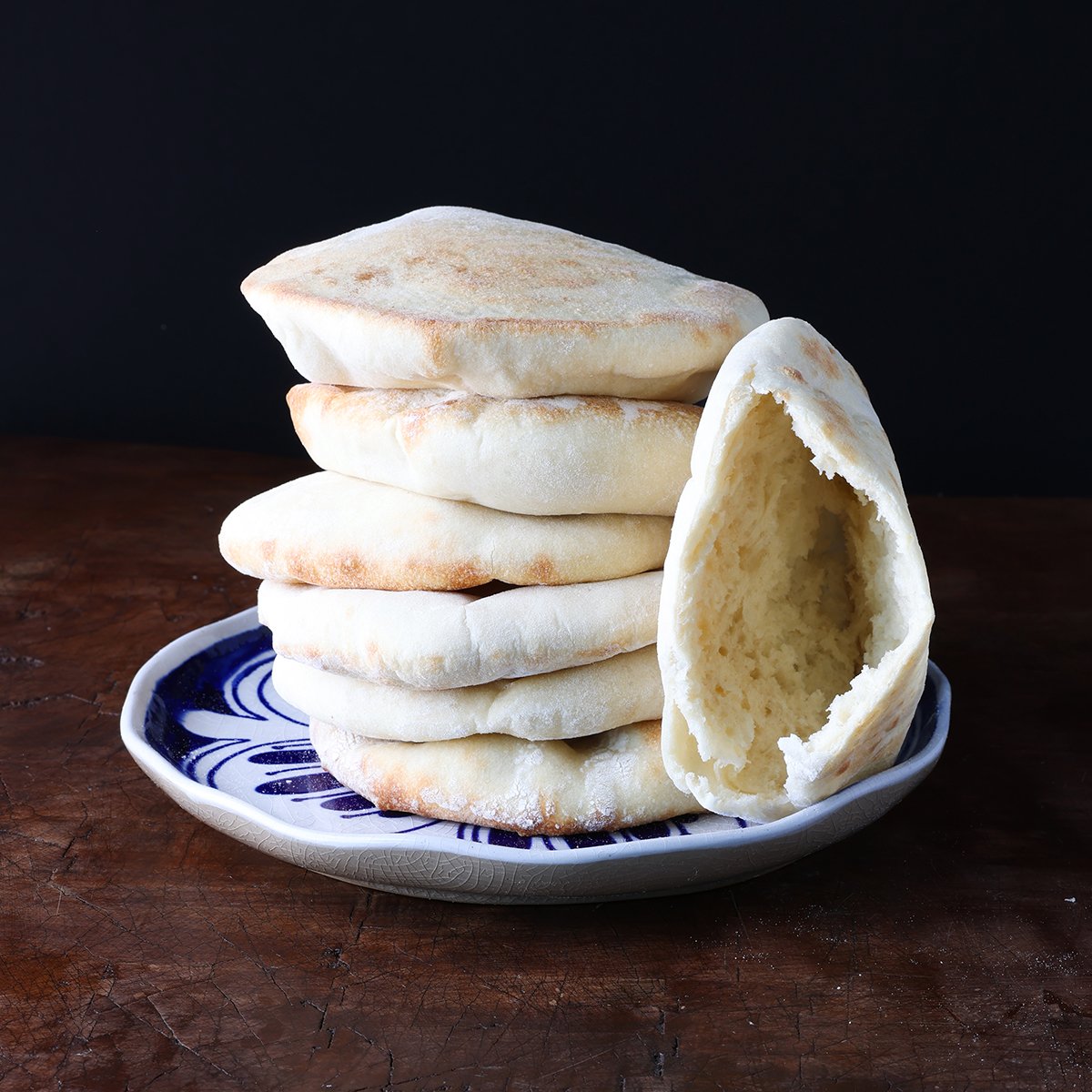 A pita pocked sliced into to show the inside bread leaning against a stack of pitas on a blue plate.