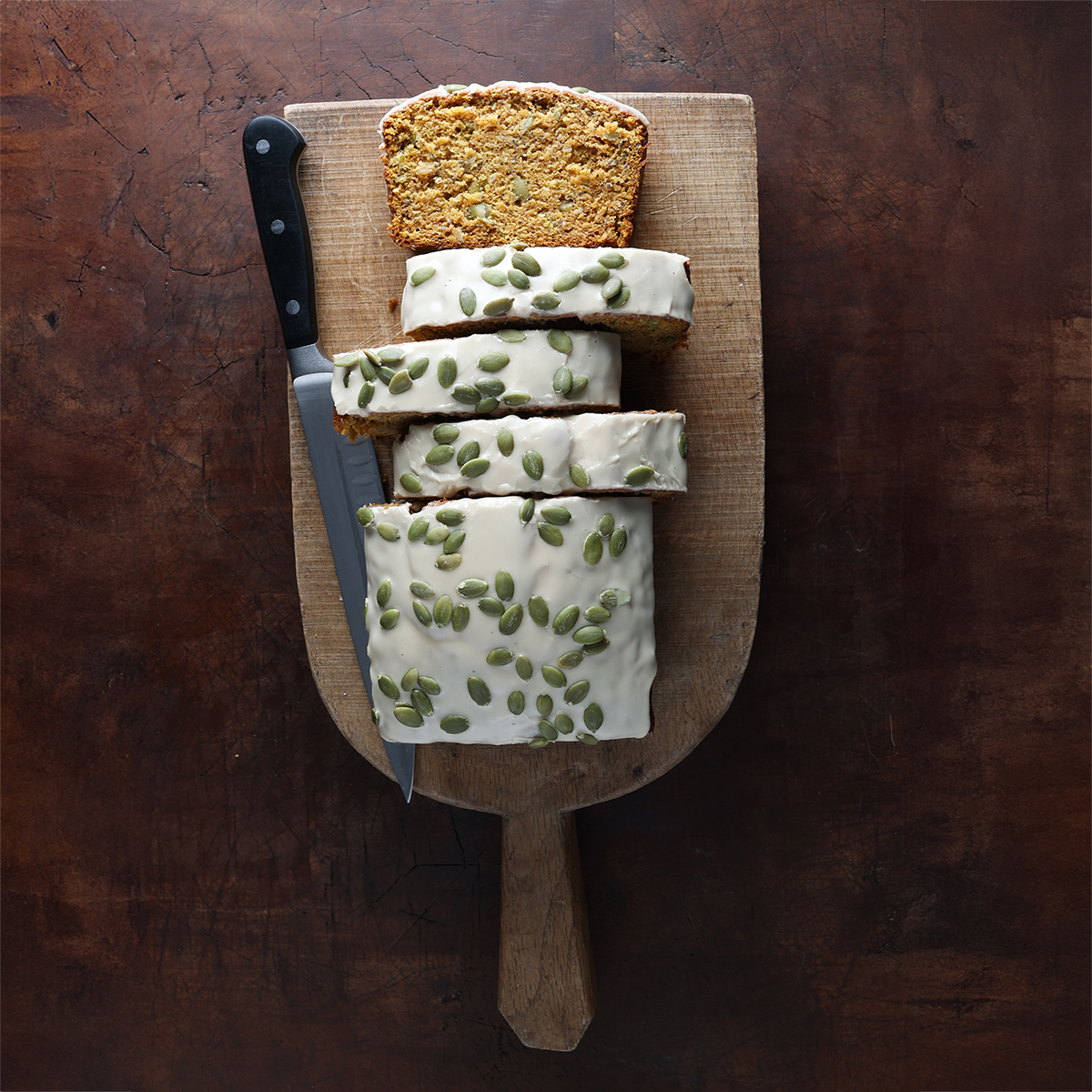 Thick slices of pumpkin banana bread topped with a maple glaze offset on a wooden serving block.