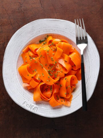 Chopped chives sprinkled over a carrot ribboned salad with a fork on the edge of the plate.