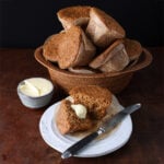 Basket of apple bran muffins behind a small plate with a butter muffin that's split in half.