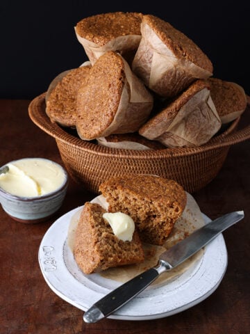 Basket of apple bran muffins behind a small plate with a butter muffin that's split in half.