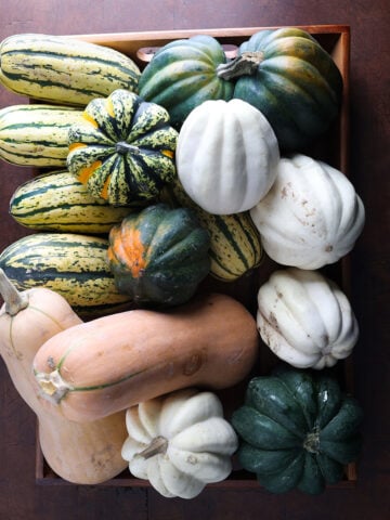 Top view of a wooden box filled with different sizes of squash in all different colors.