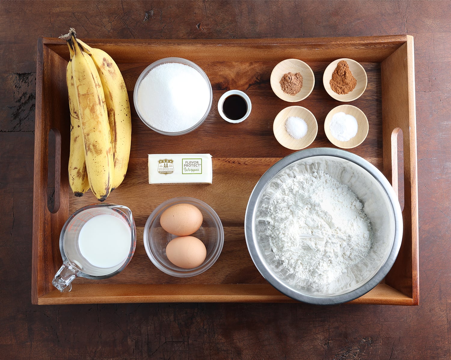Measured out ingredients laid out on a wooden tray to make jumbo banana muffins.