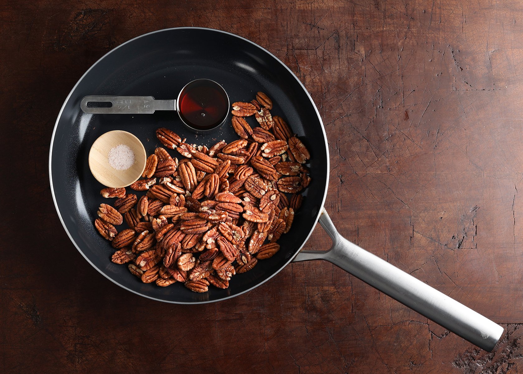 Salt and maple measured out in small dishes next to raw pecans.