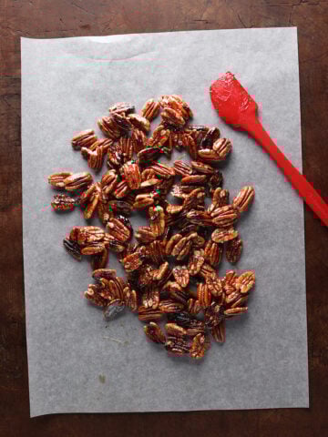 Spatula laying on glazed pecans over parchment paper.