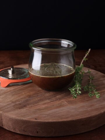 Fresh thyme laying next to a small glass bowl of maple thyme balsamic vinaigrette.