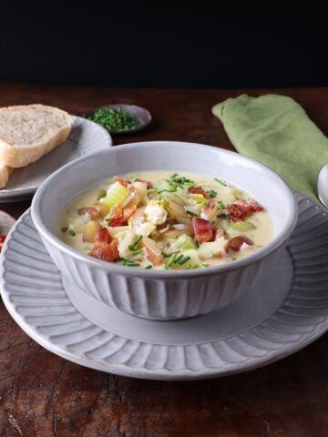 Soup bowl served with hot creamy clam chowder soup and a small plate with a couple of slices of bread on the side.