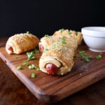 Golden brown baked pigs in a blanket with caramelized onions and topped with sesame seeds and green onions.