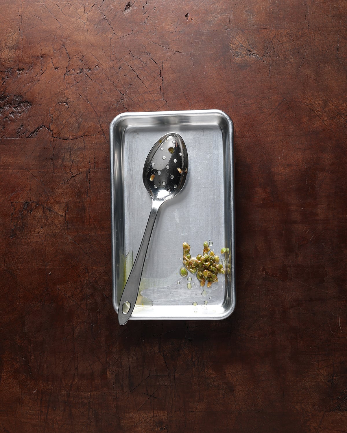Slotted spoon resting on a pan next to kumquat seeds that were removed from the fruit.