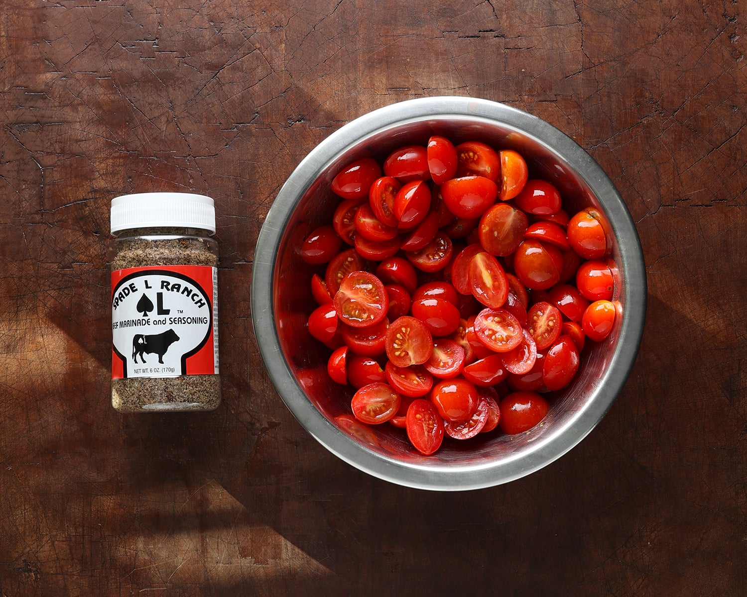 Seasoning in a jar next to a bowl of halved cherry tomatoes.