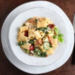 Bowl of creamy sun-dried tomato pasta with spinach on a table cropped tight to white plate