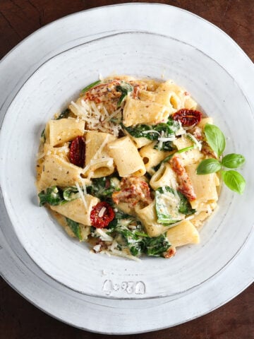 Bowl of creamy sun-dried tomato pasta with spinach on a table cropped tight to white plate