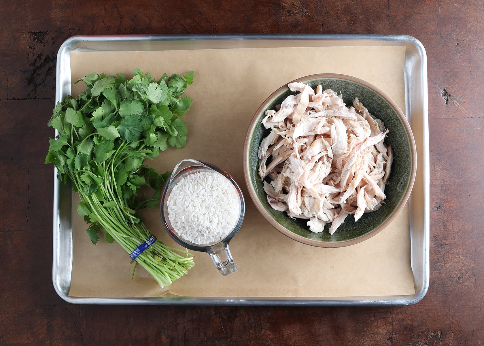 Cilantro bunch, uncooked rice in a measuring cup and shredded chicken in a bowl.