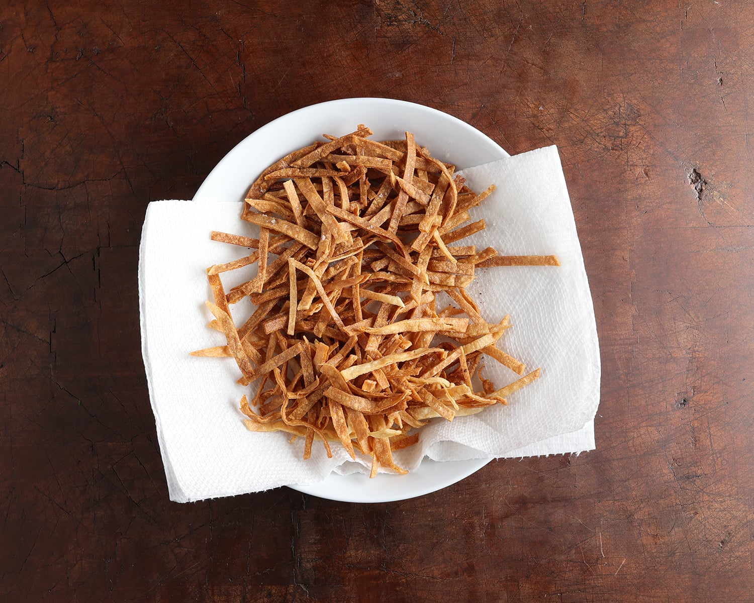 Tortilla strips resting on a papertowel lined bowl.