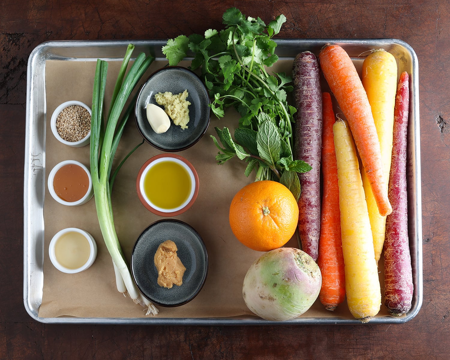 Ingredients laid out on a baking sheet that are used to prepare miso ginger ribboned carrot salad.