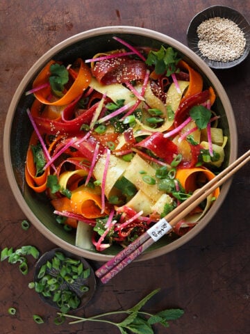 Sliced green onions on a small plate next to a bowl of miso ginger ribboned carrot salad.