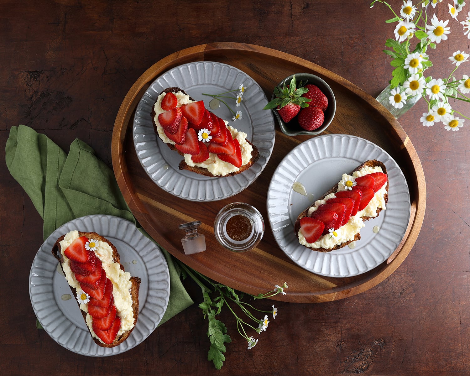 A wooden tray serving two small plates of strawberry ricotta toast and one next to the tray.