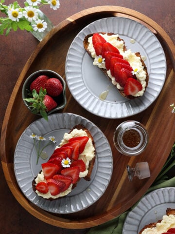 Strawberry ricotta toast served on plates on a wooden tray.