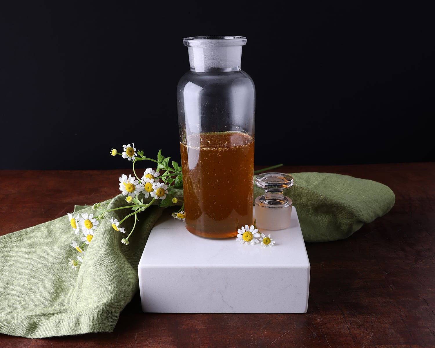 White flowers laying around the base of golden colored chamomile syrup.
