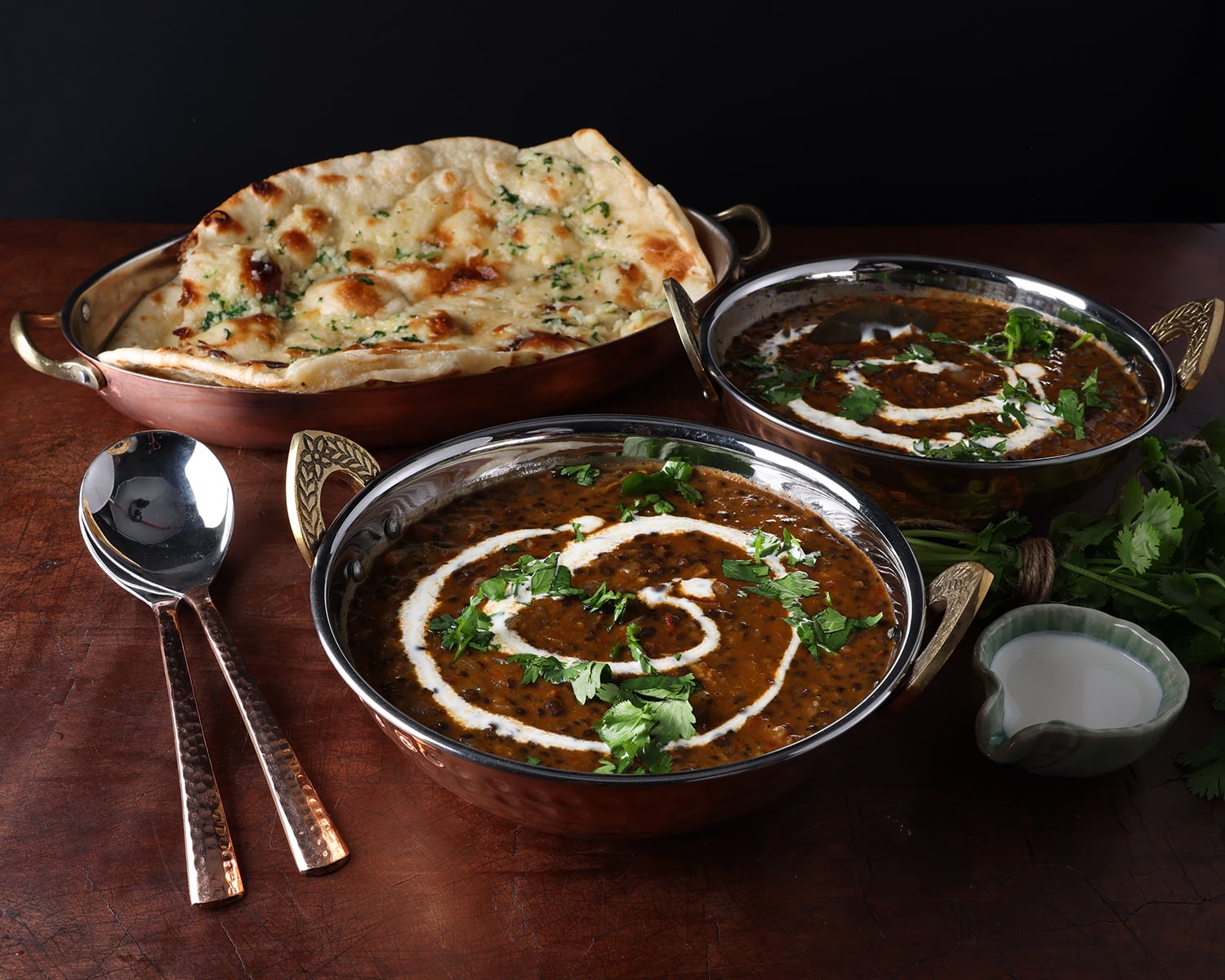 Two bowls of Dal Makhani topped with sour cream drizzled on top and a plate of naan bread to serve with it.