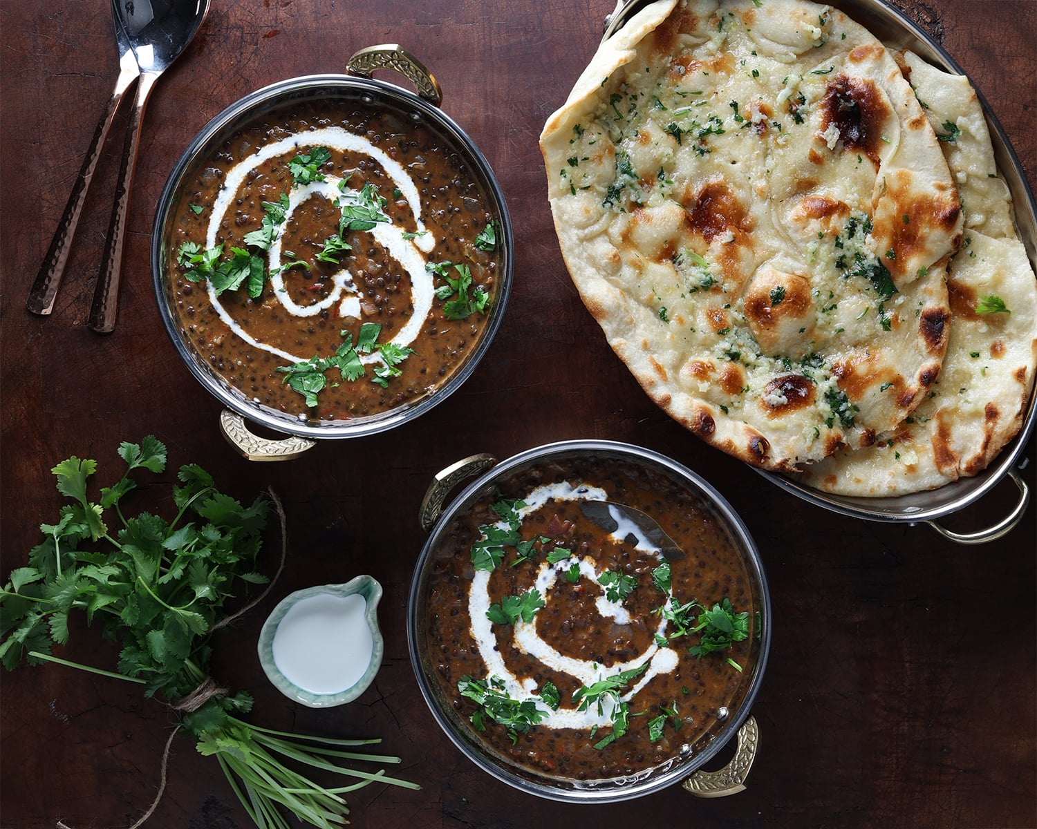 Top view of a plate with garlic naan bread and two bowls of Dal Makhani garnished with cilantro and drizzled sour cream on top.