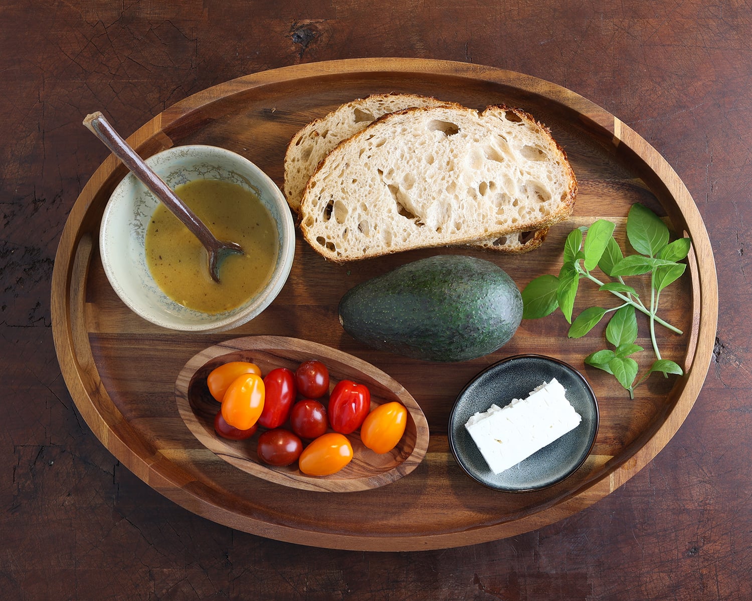 Ingredients laid out on a wooden serving tray prepare honeymoon avocado toast.