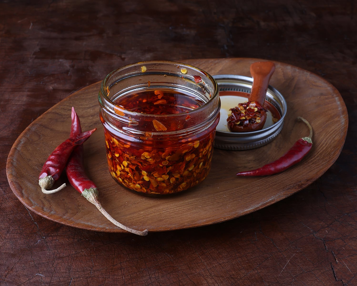 Chili de Arbol oil in a small glass jar with whole chiles laying around.