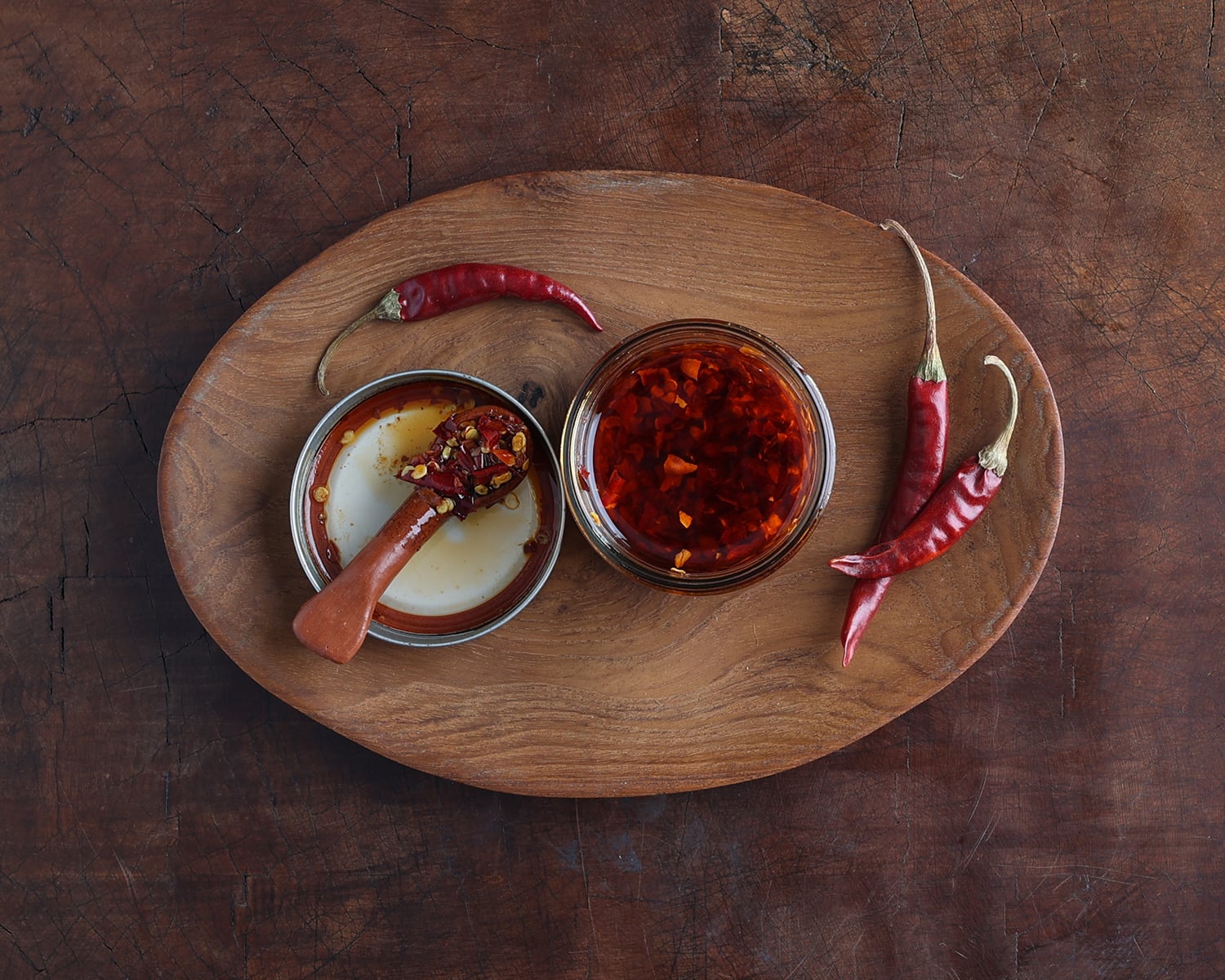 Top view of a small glass jar with the lid to the side holding chile de arbol oil with whole dried chiles next to it.