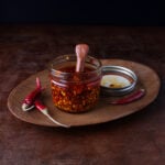 Small clay spoon resting in a glass jar of chile de arbol oil.